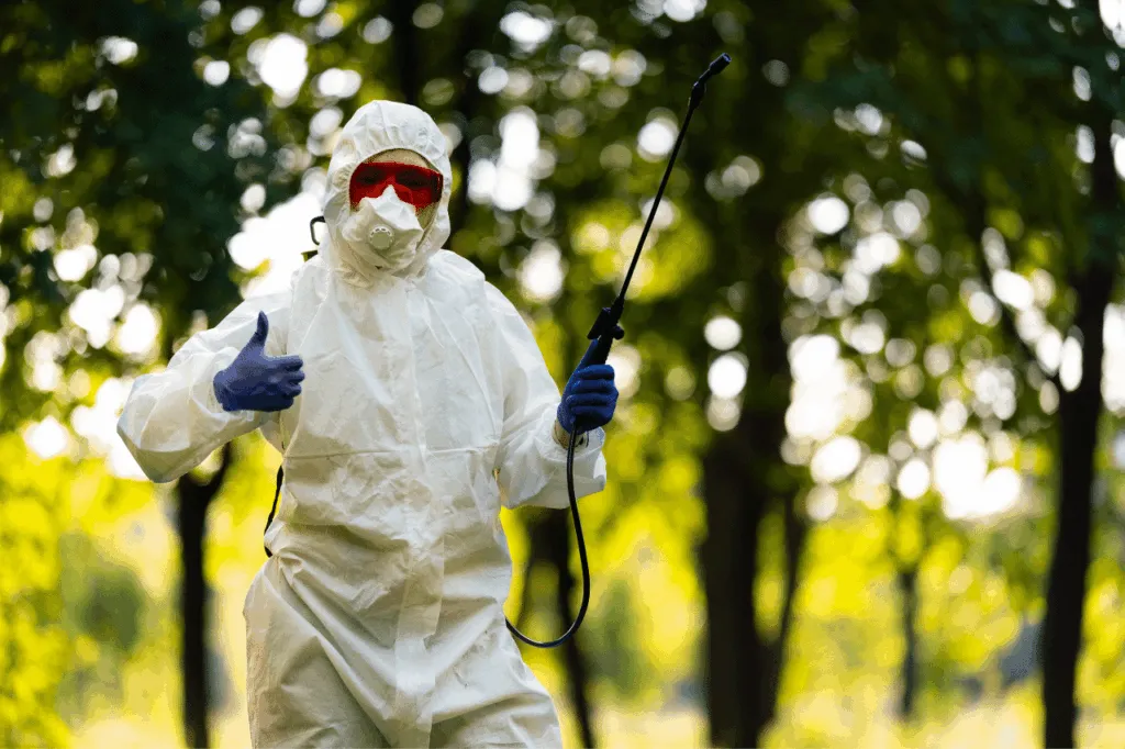 Un disinfestatore ben equipaggiato che tenendo con una mano un nebulizzatore posa davanti la fotocamera