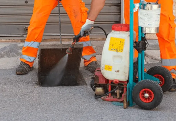 Due disinfestatori che spruzzano il prodotto per la disinfestazione con un nebulizzatore all'interno di un tombino